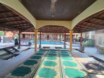 Ruang solat berbumbung dengan sejadah hijau, menghadap kolam.