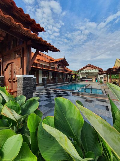 Pintu gerbang kayu dan halaman berjubin hitam putih di tepi kolam.