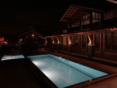 Lampu beranda menerangi barisan rumah dan kolam pada waktu malam.