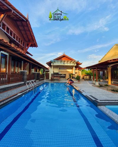 Kolam biru memanjang di antara barisan rumah pada tengah hari.
