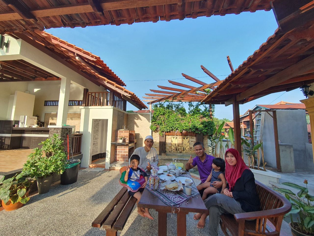 Keluarga duduk bersama di meja halaman di bawah pergola berdaun