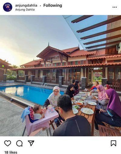 Keluarga makan di meja panjang di tepi kolam ketika matahari terbenam.