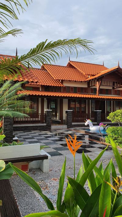 Bunga heliconia dan daun palma membingkai bumbung di tepi kolam