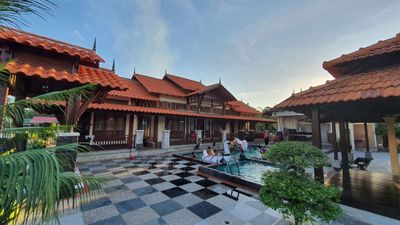 Keluarga bermain di kolam yang dikelilingi anjung dan tanaman tropika